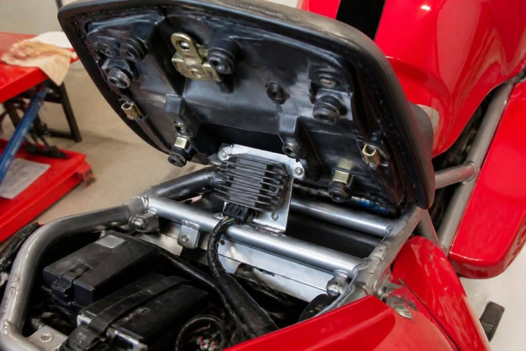 découvrez l'emplacement précis du régulateur de tension sur la ducati 916 st4 de l'année 2000, situé sous la selle passager, pour un accès facile et une maintenance simplifiée.
