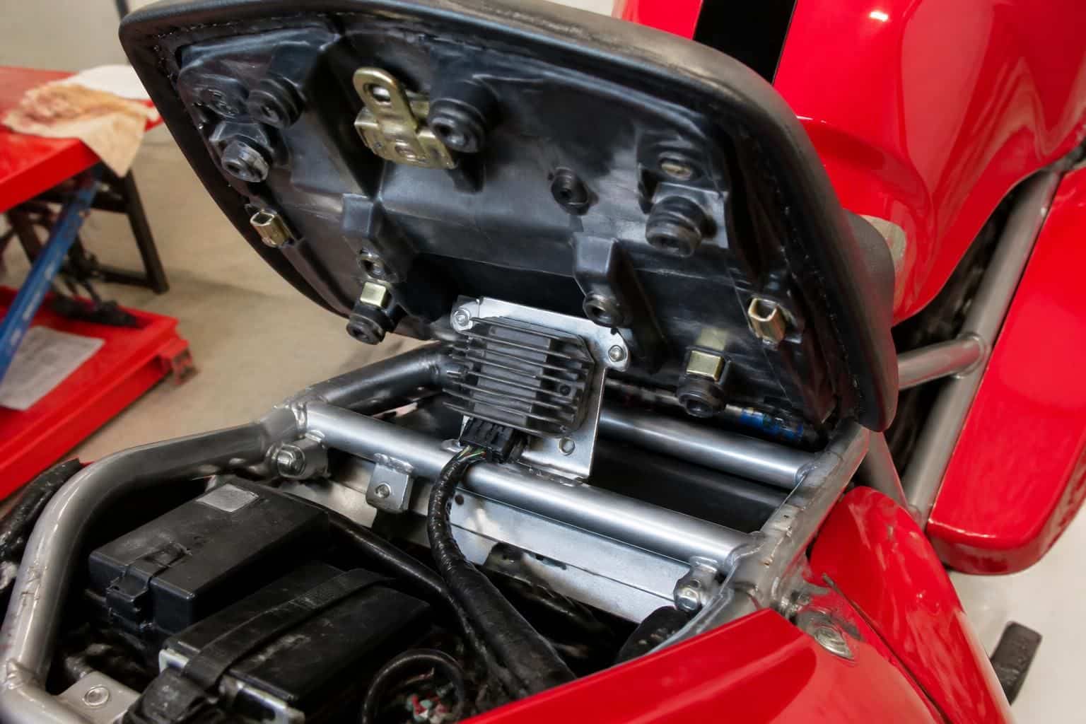 découvrez l'emplacement précis du régulateur de tension sur la ducati 916 st4 de l'année 2000, situé sous la selle passager, pour un accès facile et une maintenance simplifiée.